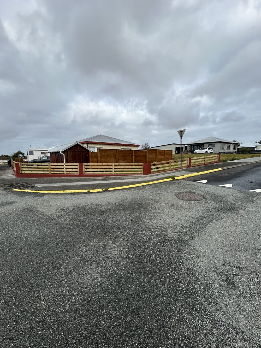 Ný timburgirðing á lóðarmörkum með rauðum steinsúlum eftir framkvæmdir